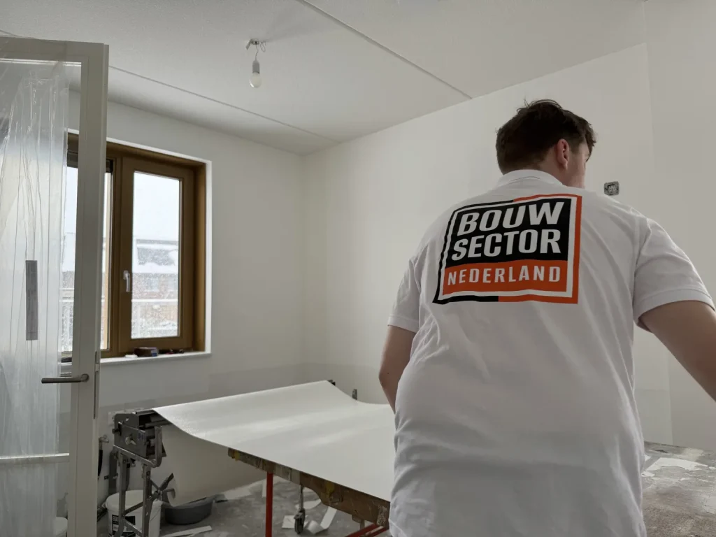 Behanger van Bouwsector Nederland trekt een baan vlies over de plaktafel in een lege kamer met houten kozijn