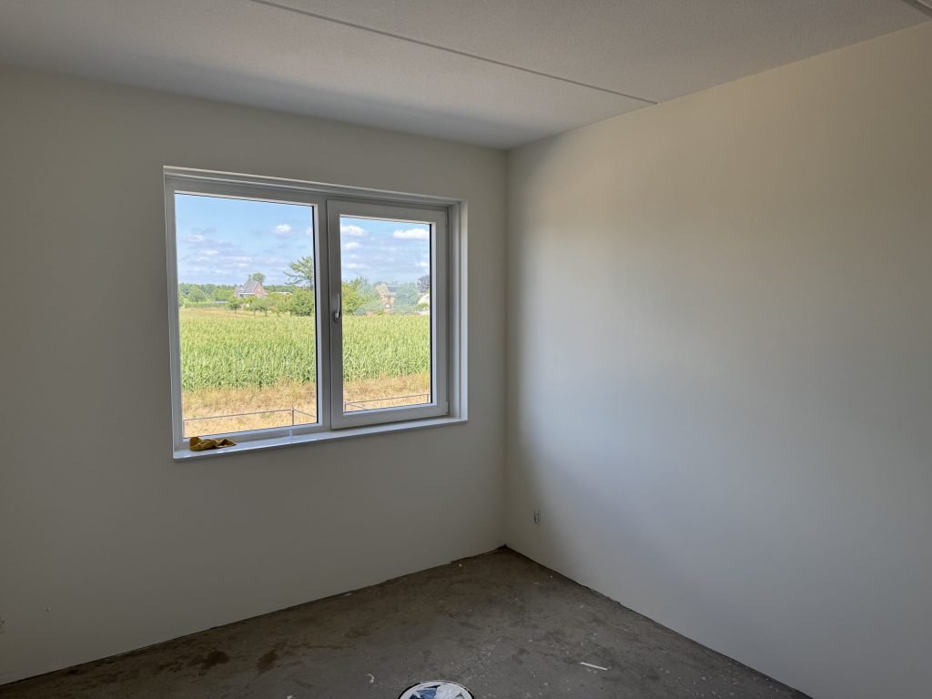 Lege slaapkamer met strakke witte wanden en een raam dat uitkijkt over het land
