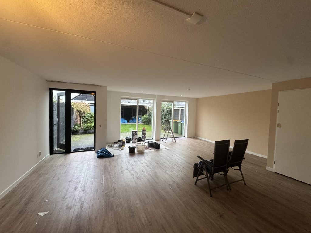 Lege doorzonkamer met houten vloer, tuindeuren en lichte wanden, klaar voor nieuw behang